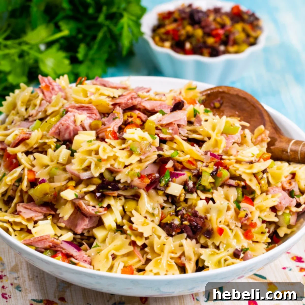 Muffaletta Pasta Salad in a bowl, with olive salad, ham, salami, and provolone cheese, dressed in vinaigrette