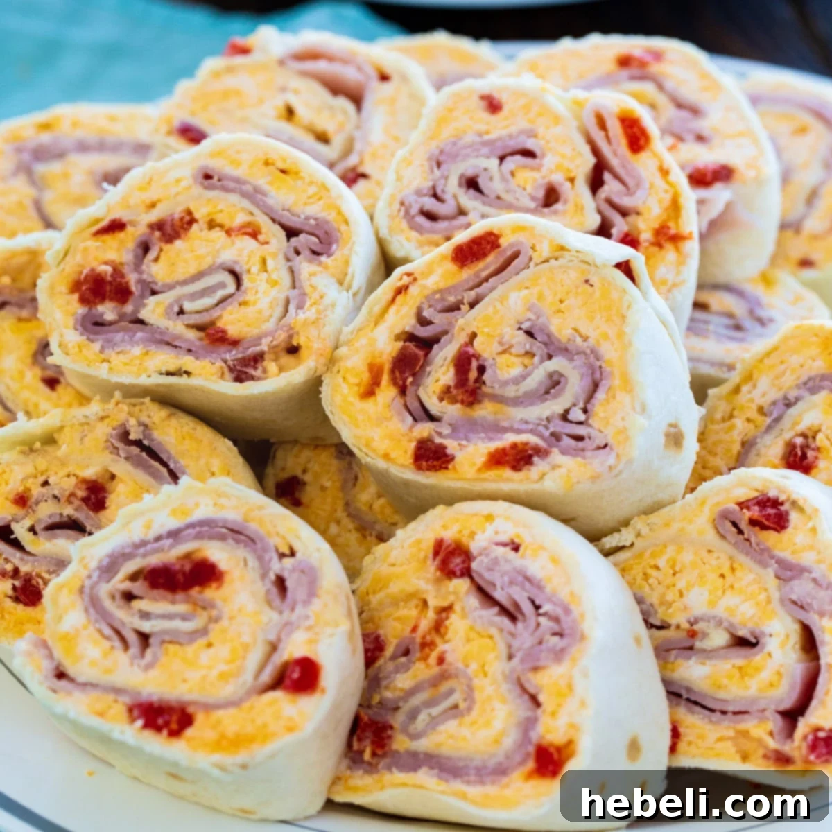 Cheesy Ham & Pimento Swirls 2 Ham and Pimento Cheese Pinwheels piled high on a white serving plate, garnished with fresh parsley.