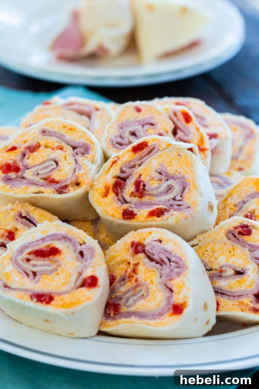 Cheesy Ham & Pimento Swirls 4 A close-up view of perfectly sliced Ham and Pimento Cheese Pinwheels, showcasing the layers of ham and creamy filling.