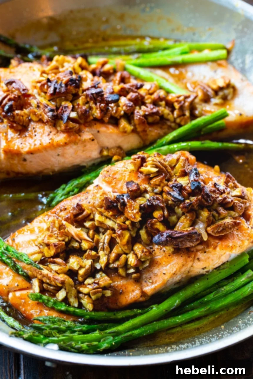 Two Bourbon Pecan Glazed Salmon fillets in a pan with tender asparagus, showcasing the glistening glaze.