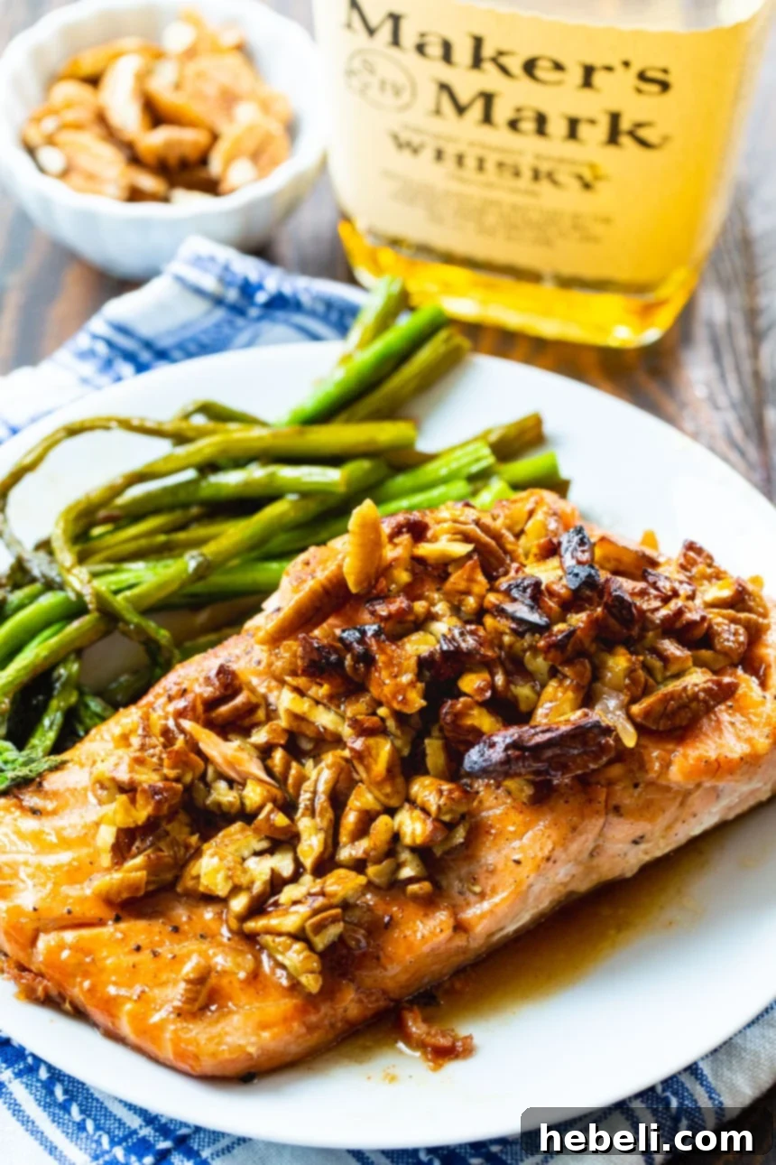 A close-up of a perfectly cooked salmon fillet with bourbon-pecan glaze on a white plate, garnished with fresh asparagus.