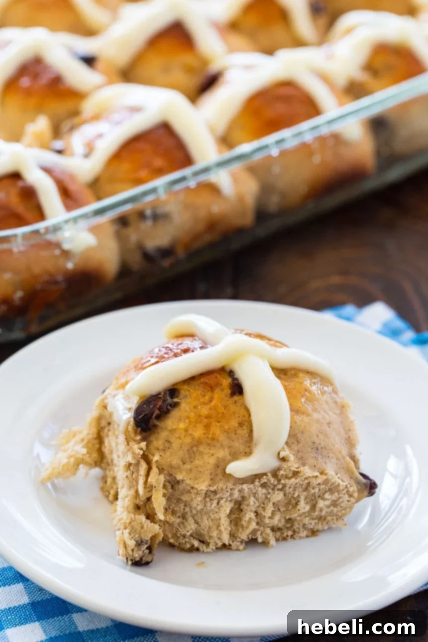 A single Hot Cross Bun on a white plate, showing its soft interior and perfect glaze.