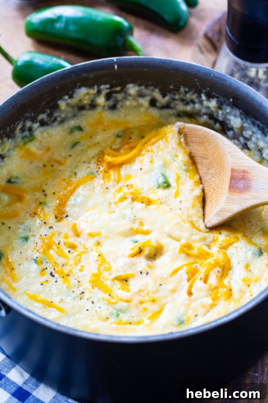 Jalapeno Cheddar Grits Delight 3 Close-up of creamy Jalapeno Cheddar Cheese Grits in a bowl, garnished with a fresh jalapeno slice.