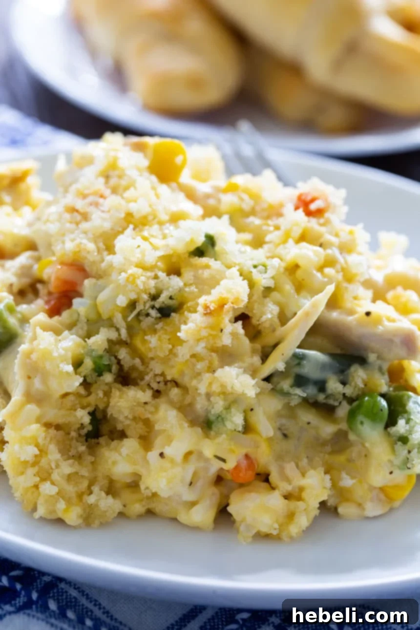 Velvety Chicken and Rice Casserole 4 Creamy Chicken and Rice Casserole on a white plate with crescent rolls in background.