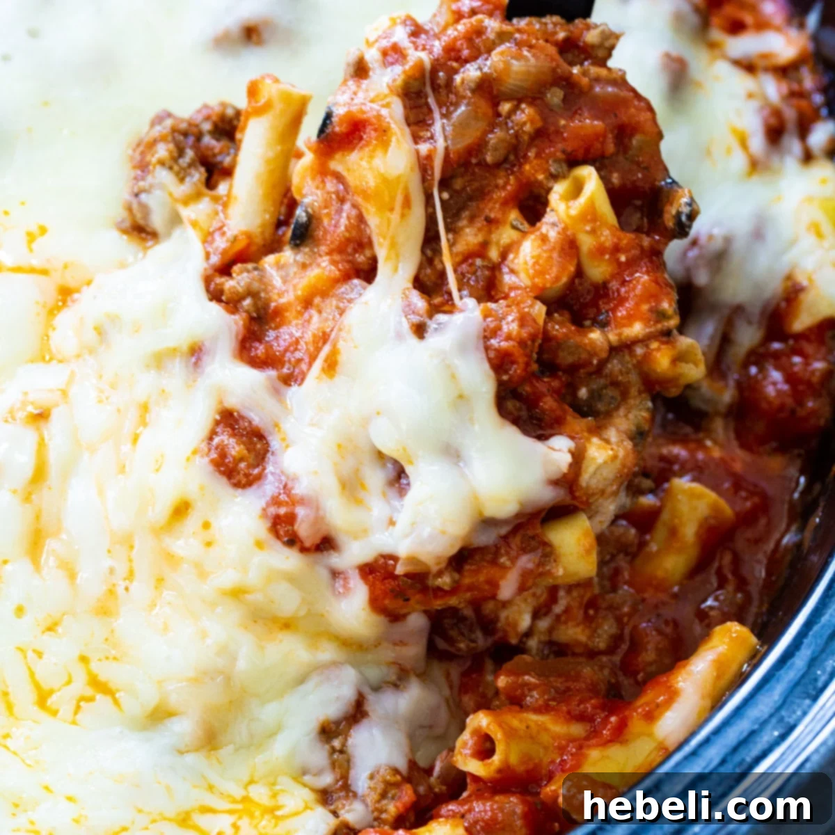 A spoon scooping perfectly cooked Crock Pot Baked Ziti, rich with meat and melted cheese, directly from the slow cooker.