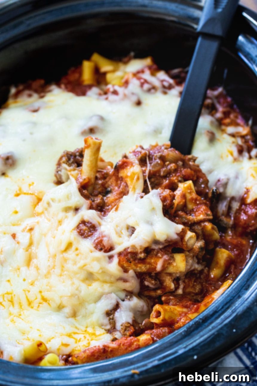Close-up of Crock Pot Baked Ziti being scooped with a serving spoon from a black slow cooker, highlighting the rich texture.