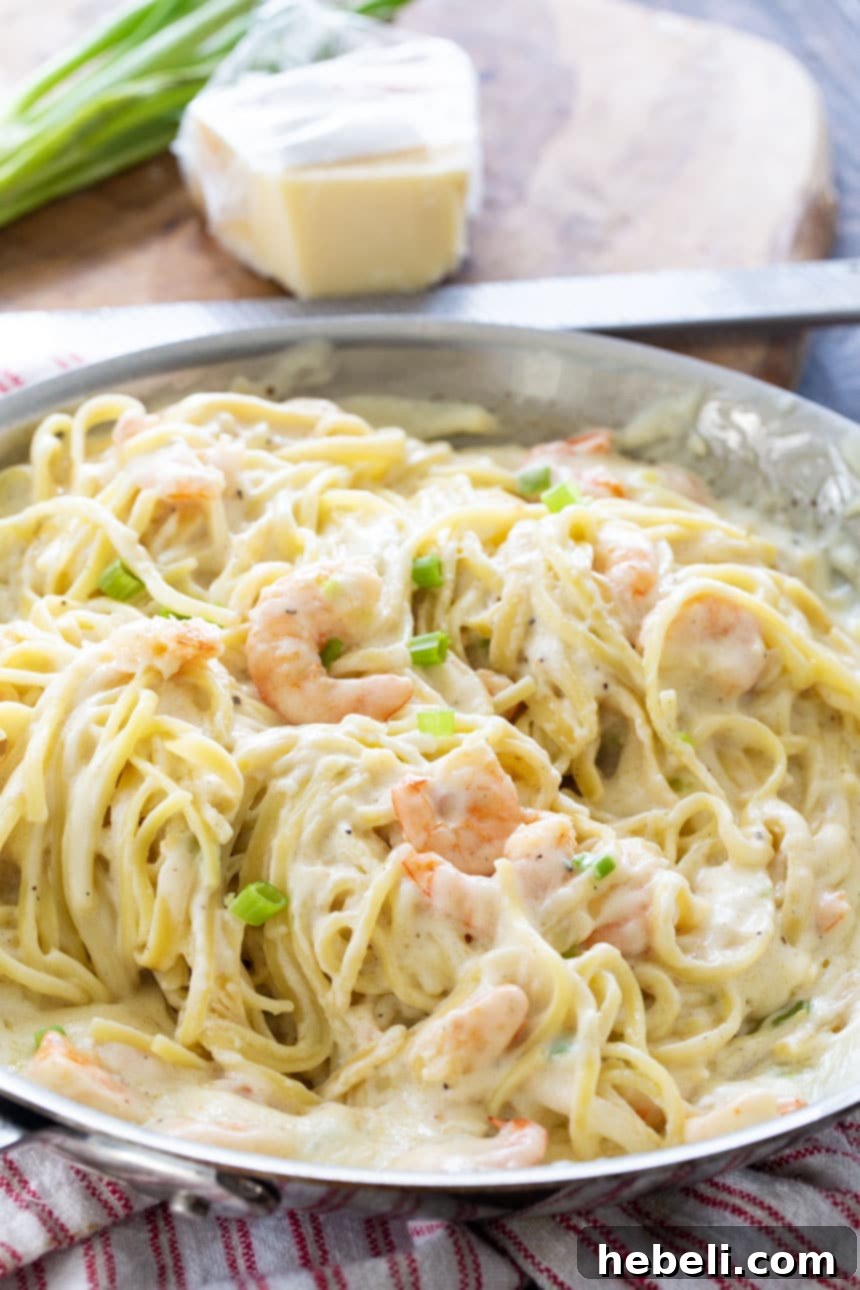 Close-up of Cheesy Garlic Shrimp Alfredo in a pan with Parmesan cheese in the background, showcasing its rich and creamy texture.