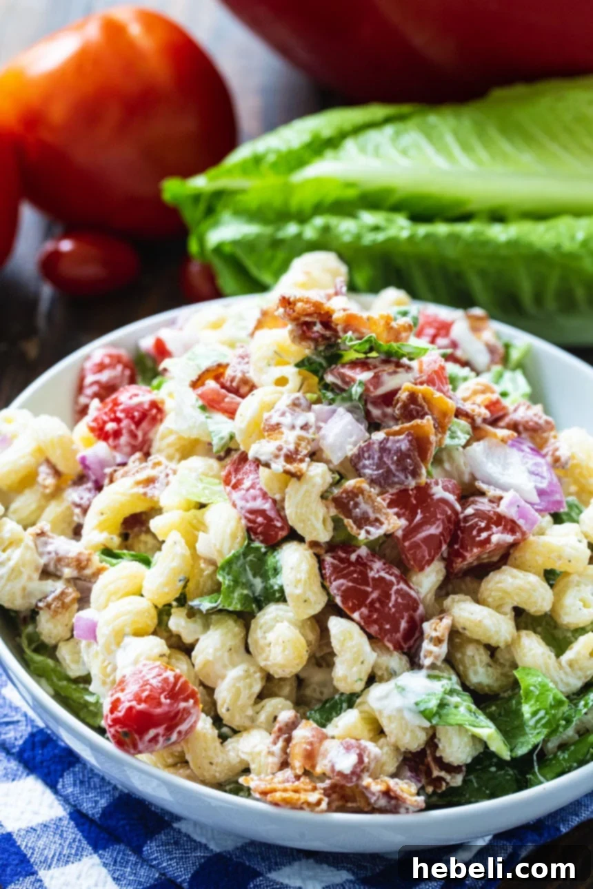 BLT Pasta Salad with a focus on fresh tomatoes and crisp lettuce in the background, highlighting its key ingredients.