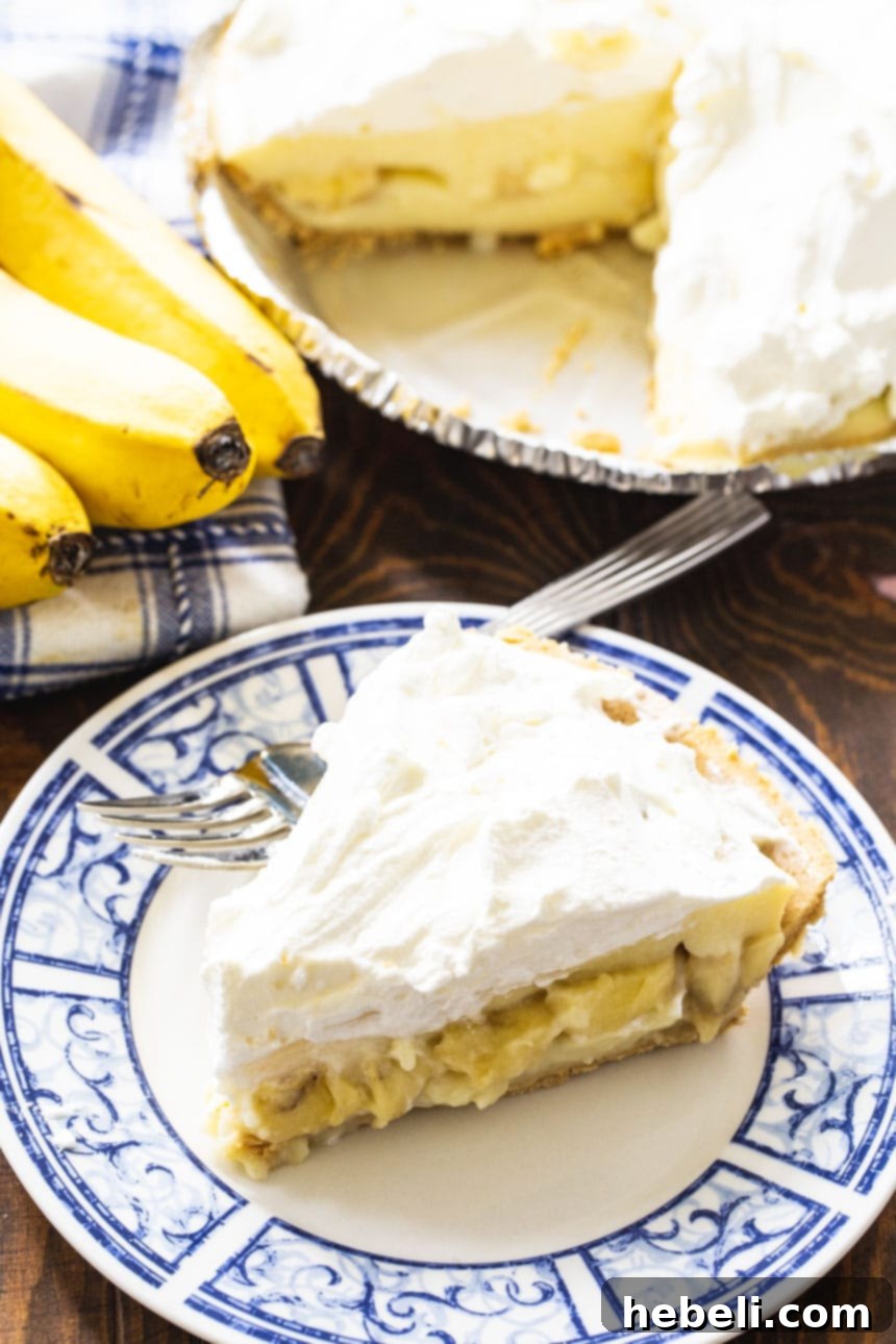 A tempting slice of homemade Banana Cream Pie, with fresh bananas visible within the creamy layers and a dollop of whipped cream on top, against a backdrop of whole bananas.