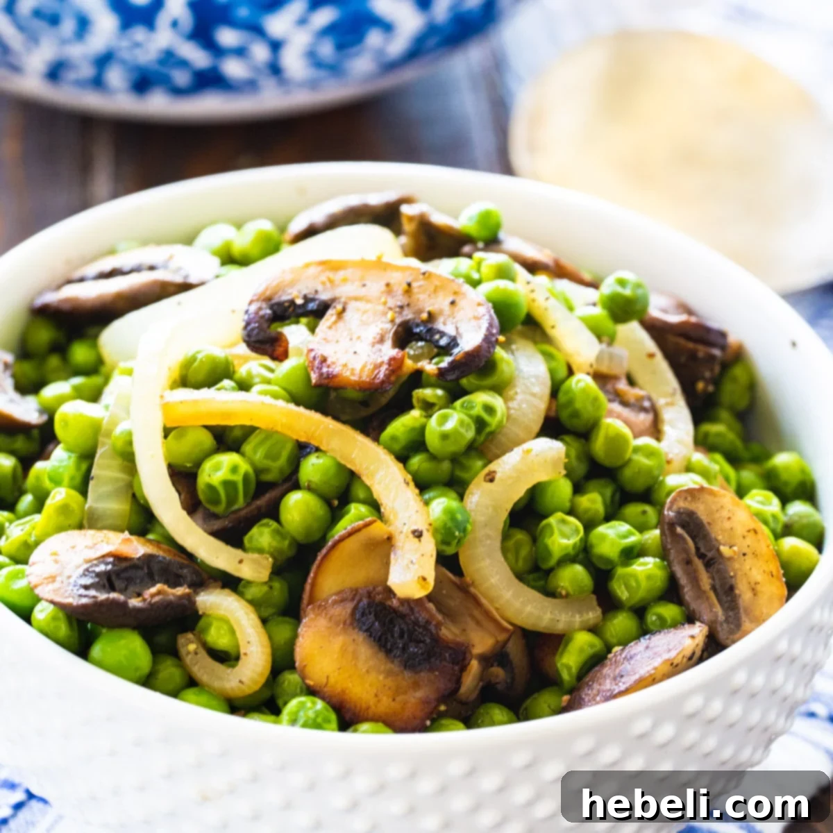 A serving of Buttery Peas and Mushrooms in a elegant white bowl, showcasing their vibrant green color and savory brown mushrooms.