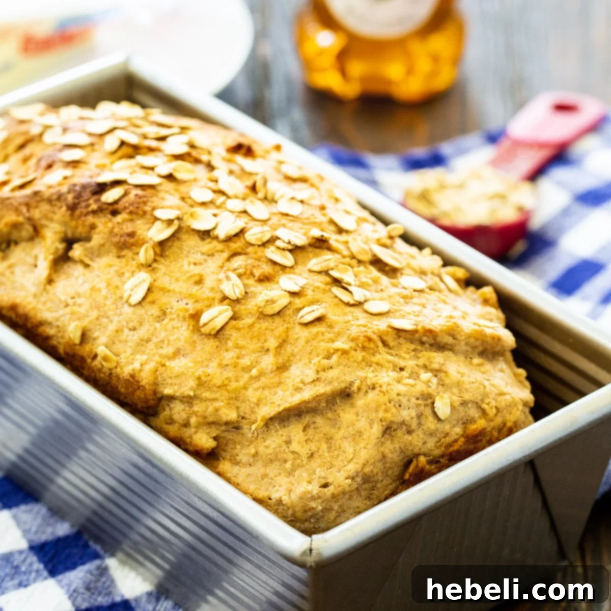 Golden Honey Oat Loaf 2 A freshly baked loaf of Honey Oat Wheat Bread, golden brown and sprinkled with oats, sitting in a metal loaf pan.