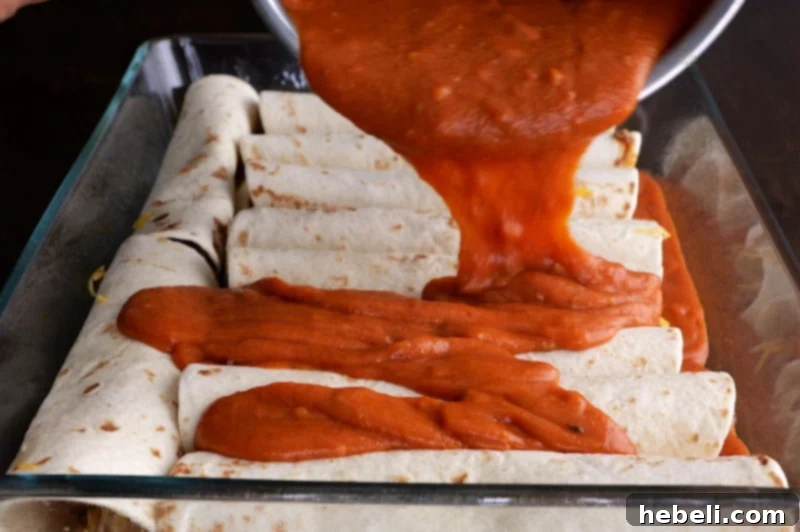 Kıymalı Enchilada 7 Pouring red sauce over assembled enchiladas in a baking dish.