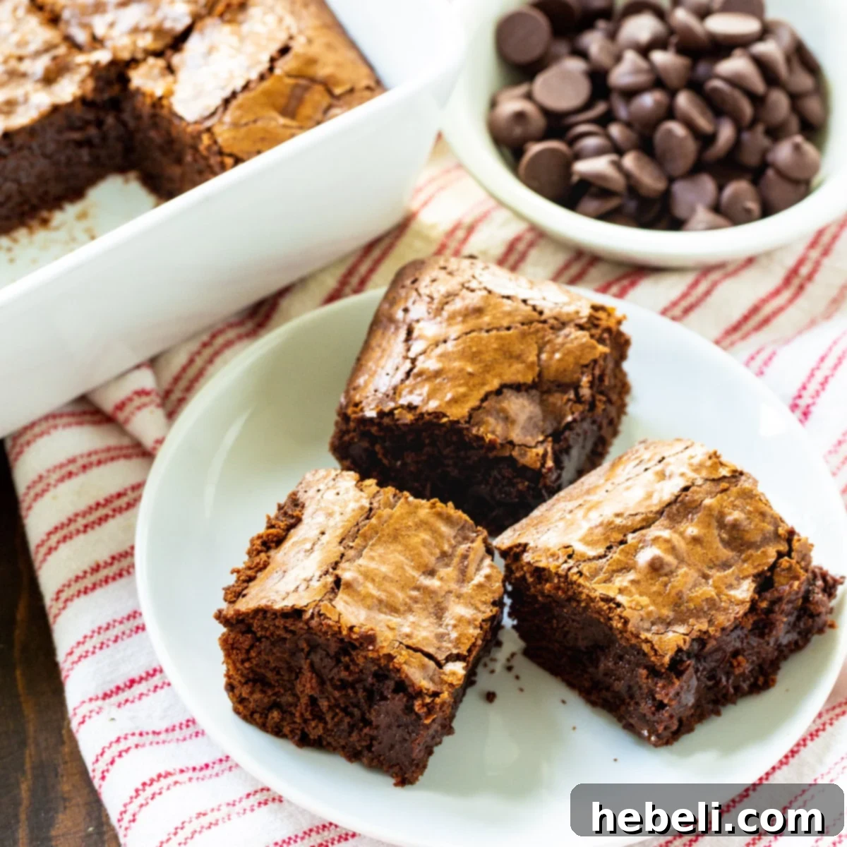 Three perfectly fudgy Bittersweet Chocolate Brownies artfully arranged on a pristine white plate, showcasing their rich color and slightly crackled tops.