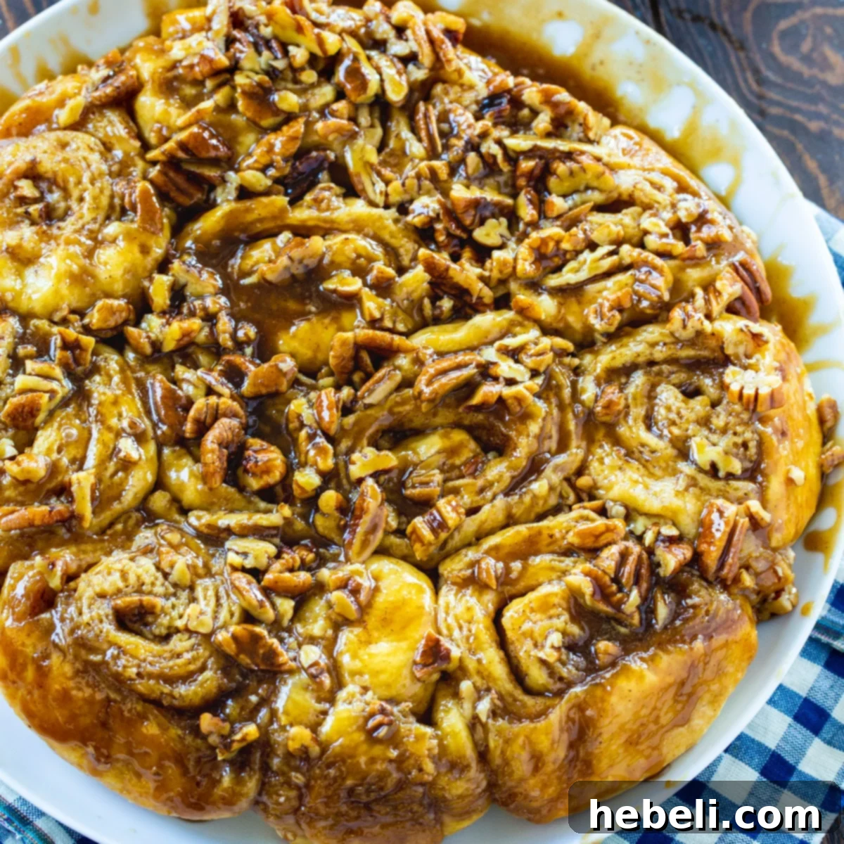 A plate of freshly baked Bourbon Pecan Cinnamon Rolls, glistening with caramel sauce and topped with pecans.