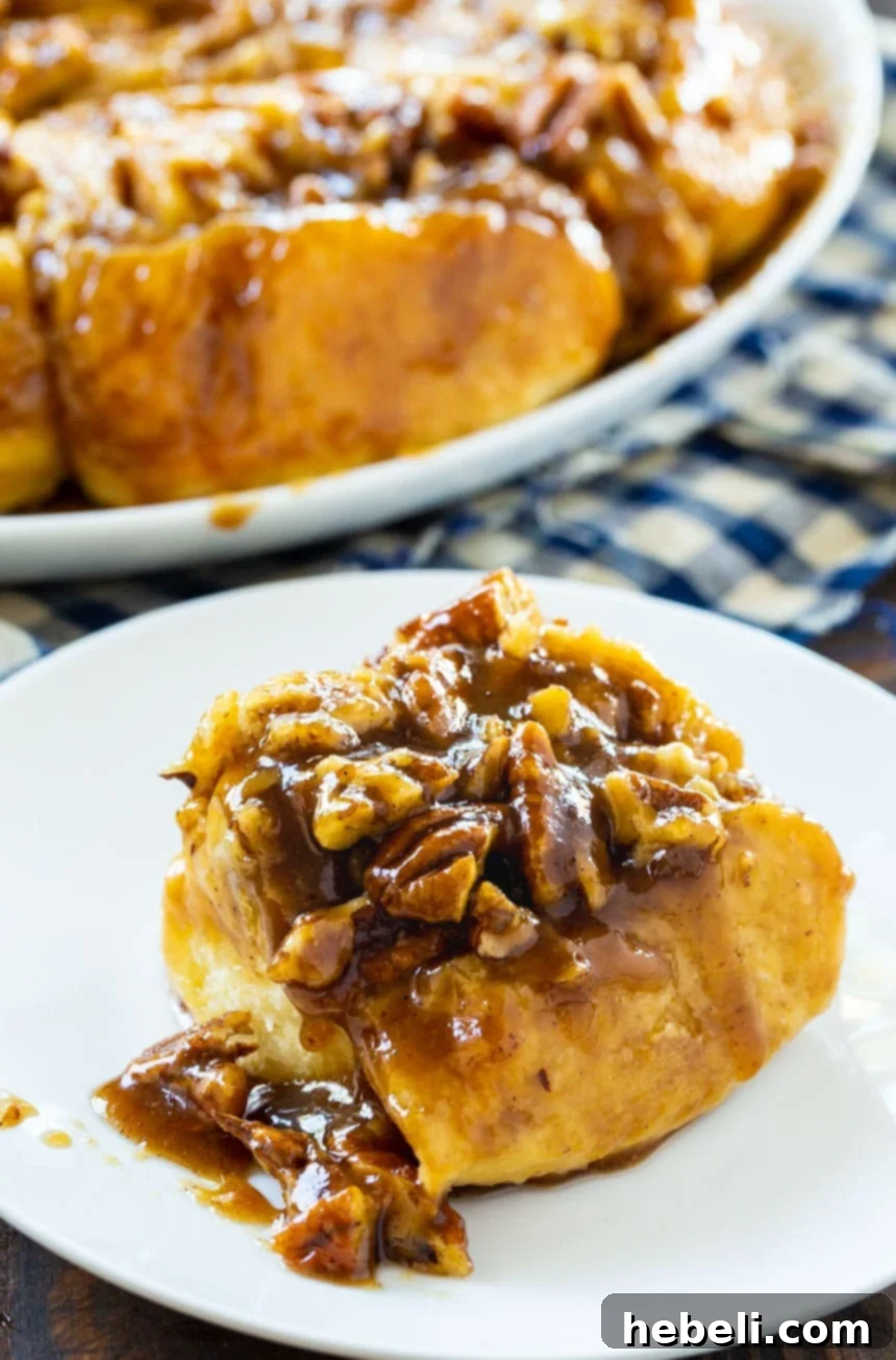 A single Bourbon Pecan Cinnamon Roll on a small white plate, showing the rich caramel and pecans.