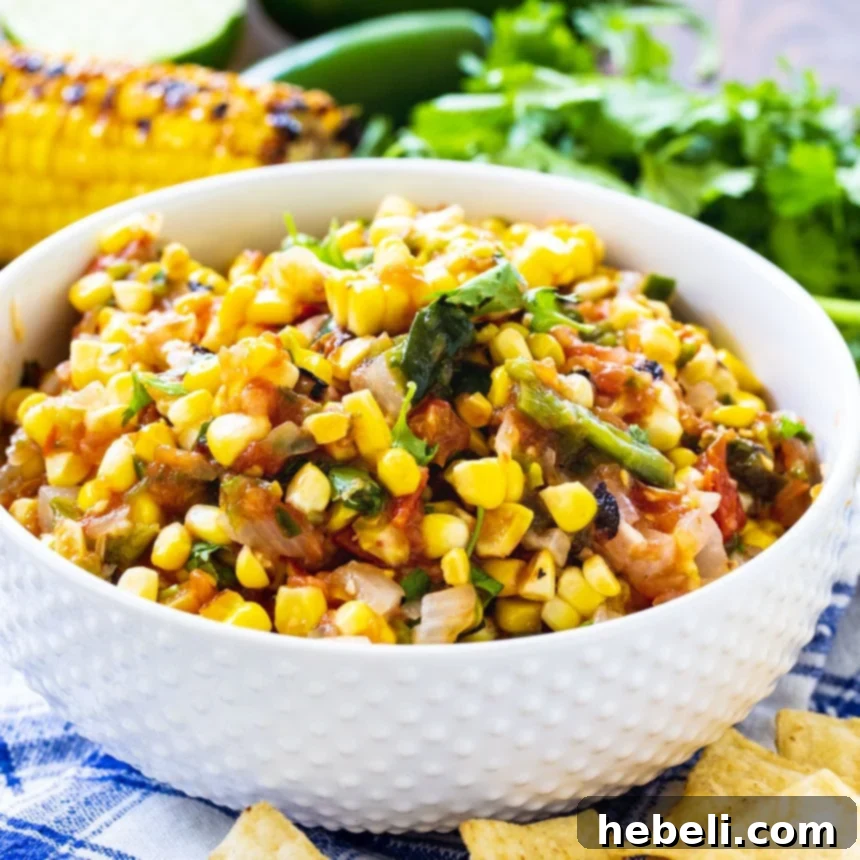Bright and colorful roasted corn salsa in a white bowl, surrounded by crispy tortilla chips and fresh cilantro sprigs, ready to be enjoyed.