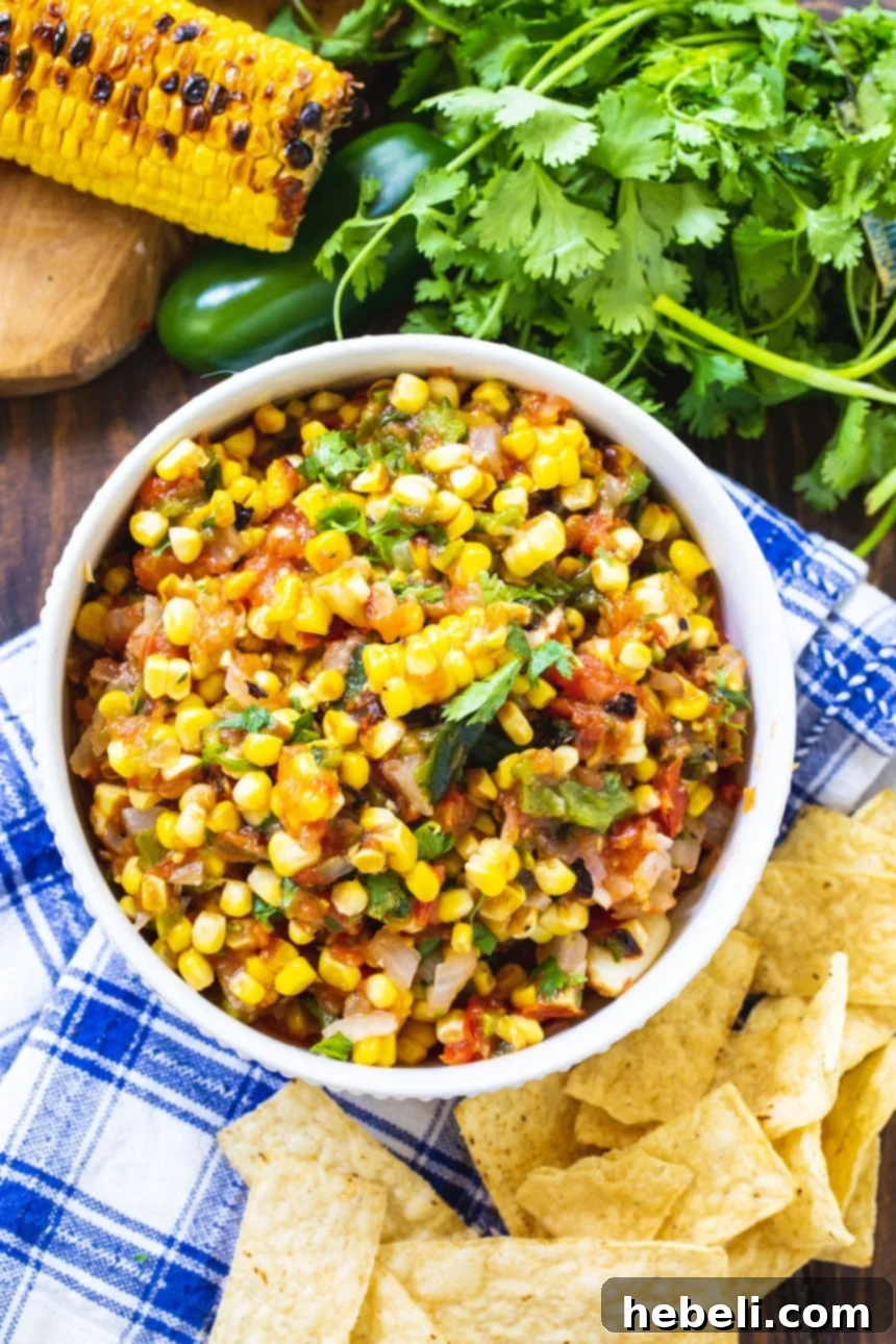 A top-down view of roasted corn salsa served in a white bowl, garnished with fresh cilantro and surrounded by golden tortilla chips.