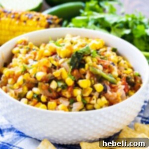 Corn salsa in a white bowl surrounded by tortilla chips and cilantro.