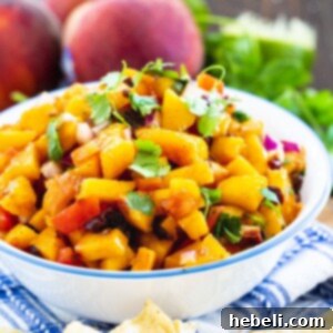 Peach Salsa in a bowl surrounded by fresh peaches and cilantro.