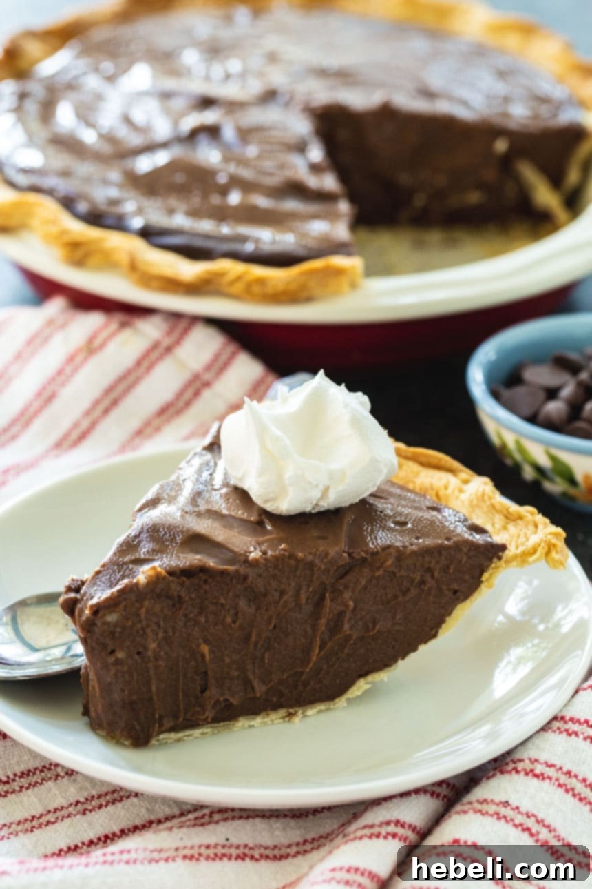 A perfectly sliced piece of Dark Chocolate Pie on a plate, with the rest of the pie in the background.