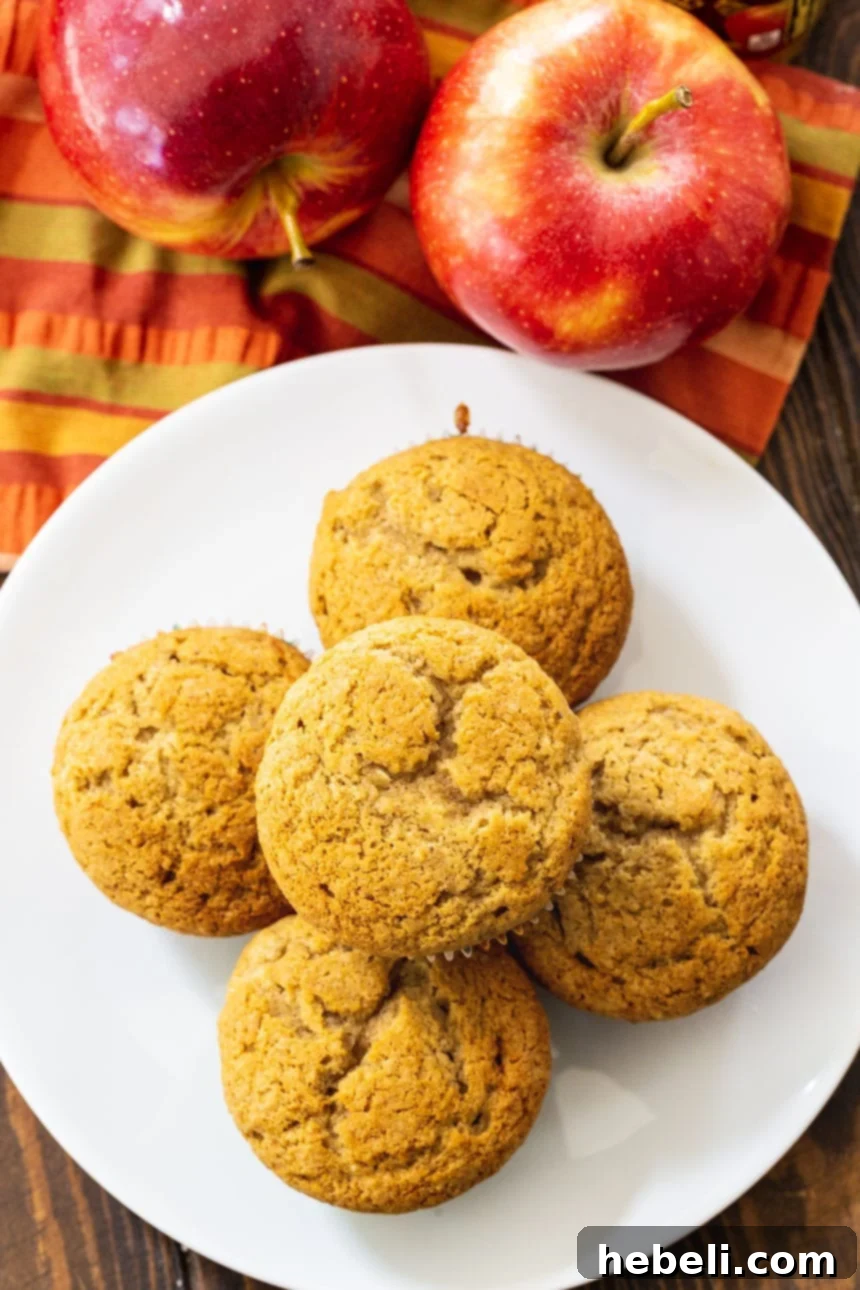 An overhead shot of several Apple Butter Muffins cooling on a white plate, showcasing their inviting golden-brown tops.