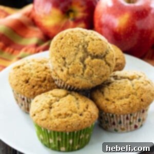 Muffins on a white plate with fresh apples in the background, hinting at the key ingredient.