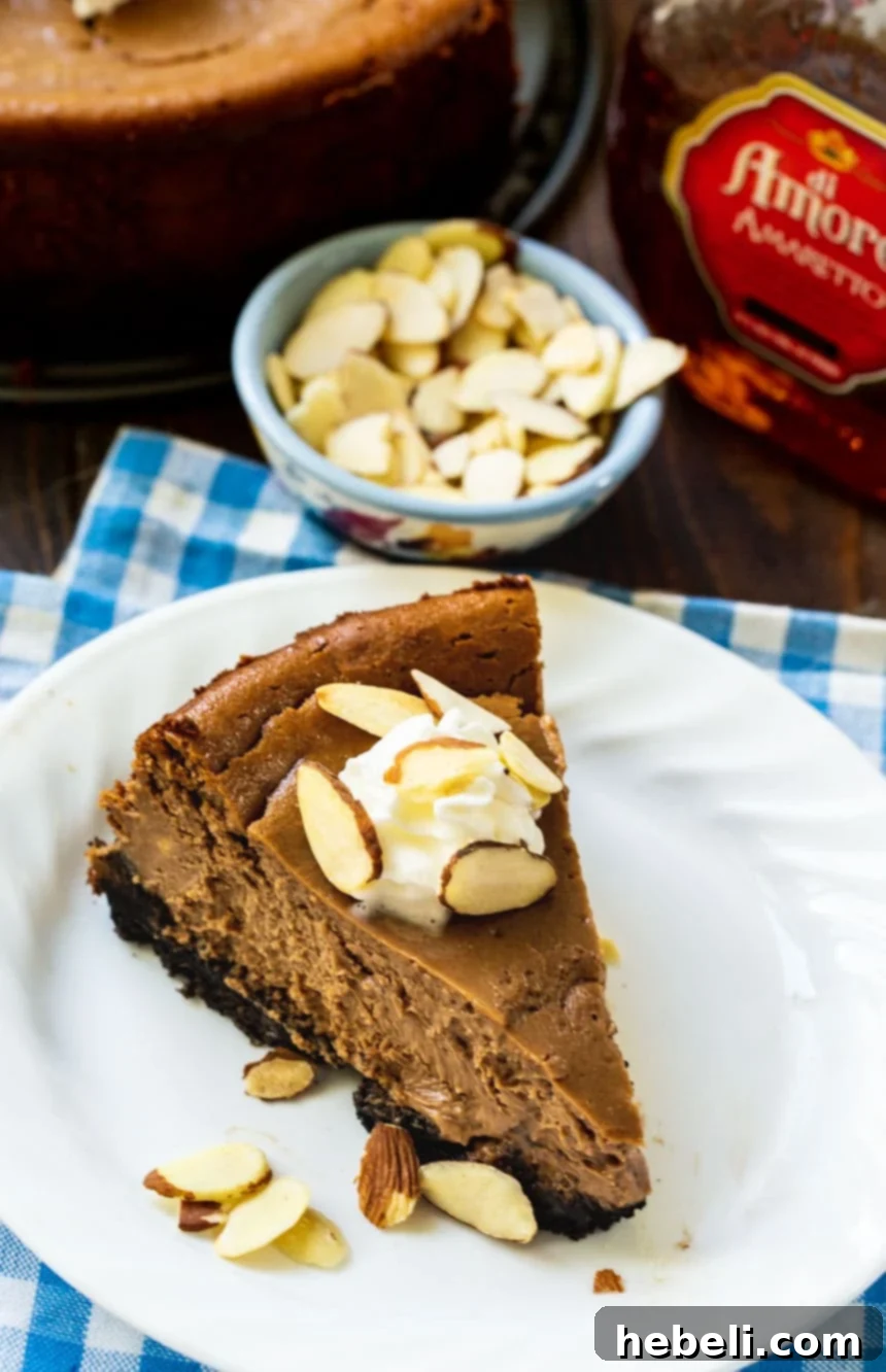 A delightful slice of Chocolate Amaretto Cheesecake served on a pristine white plate, accompanied by a small bowl of crunchy almonds, highlighting its rich texture and inviting presentation.
