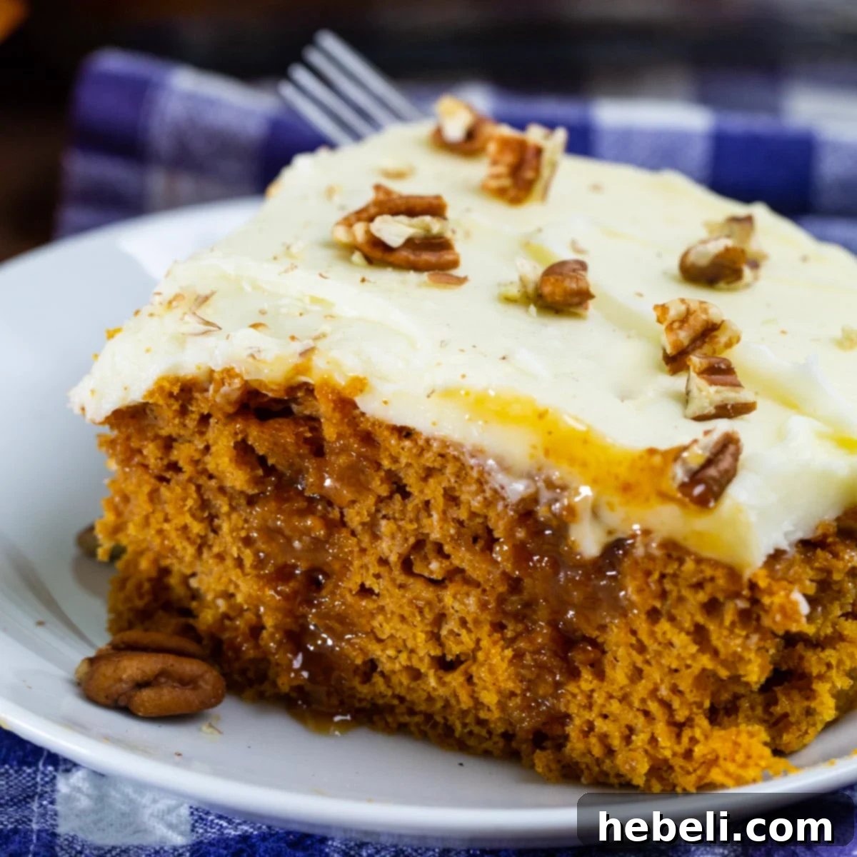 A delectable slice of Pumpkin Caramel Poke Cake on a white plate, showcasing its layers of spiced cake, caramel drizzle, and thick cream cheese frosting, garnished with pecans.