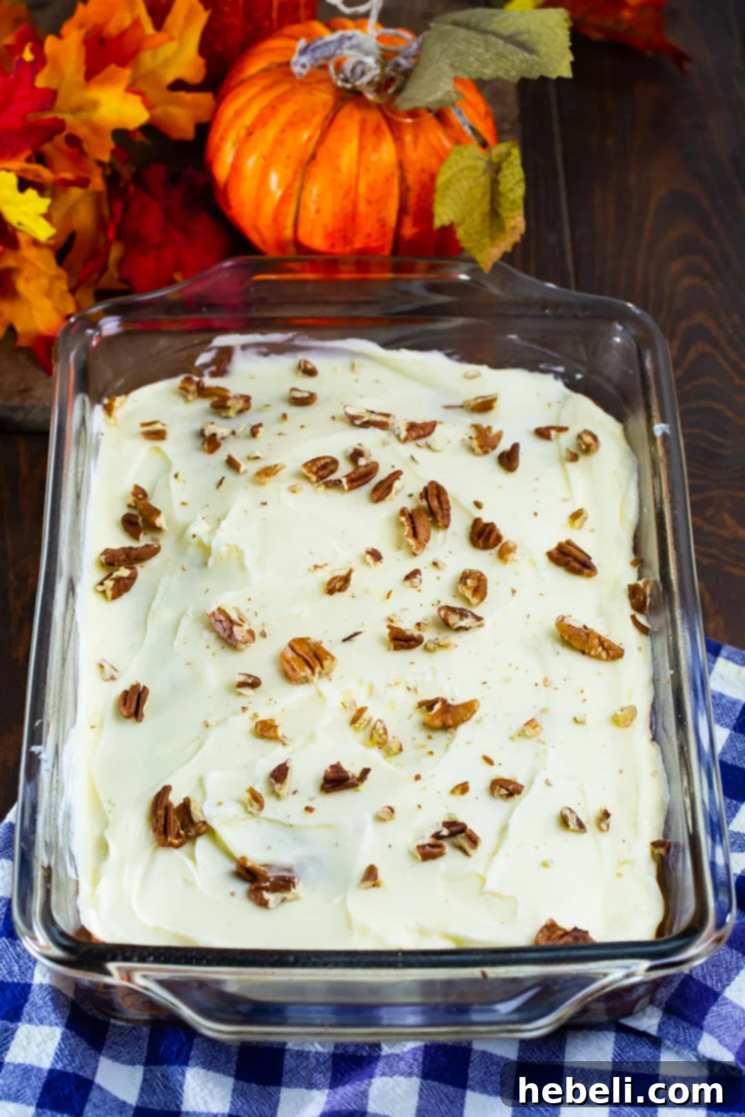 A whole Pumpkin Caramel Poke Cake, baked in a 9x13-inch baking dish, ready to be sliced and served, topped with creamy frosting and nuts.