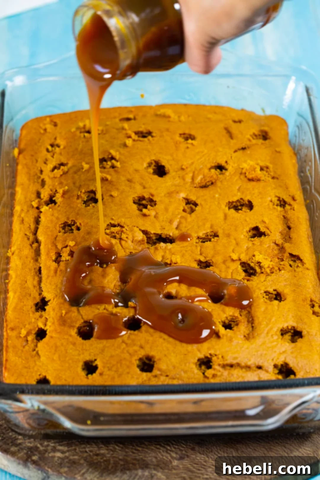 Caramel sauce being poured over the poked holes of a pumpkin cake, ready to soak in and create a moist, flavorful dessert.
