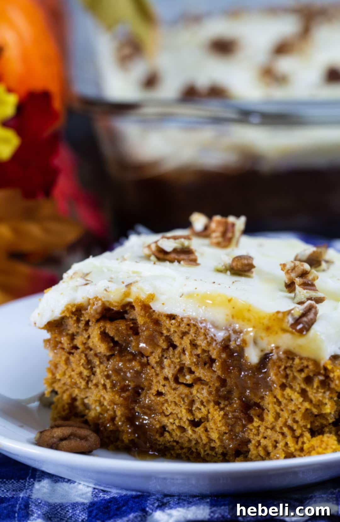 A close-up of a slice of Pumpkin Caramel Poke Cake on a plate, showing the moist cake, caramel, and fluffy cream cheese frosting.
