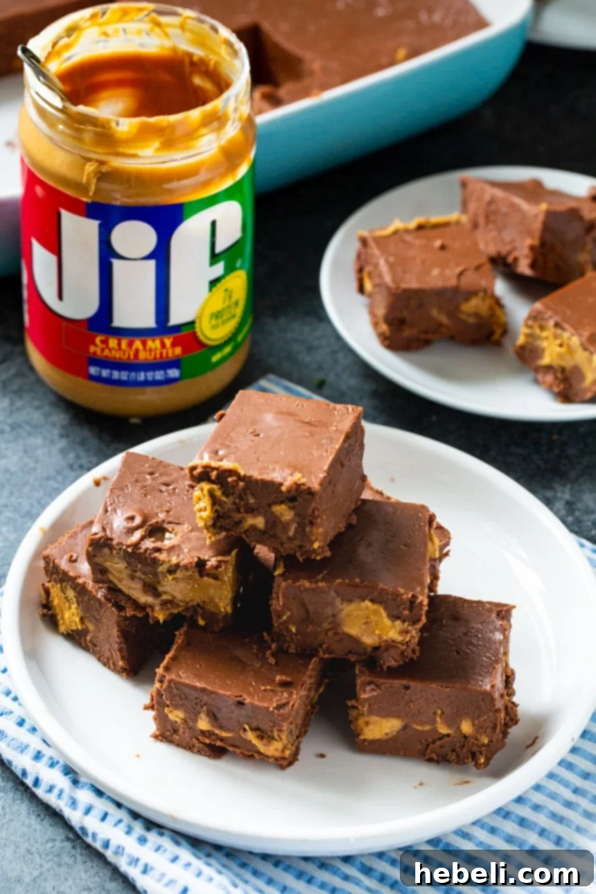 Decadent Peanut Butter Chocolate Fudge 3 Squares of fudge on a plate with a jar of peanut butter in the background, highlighting the ingredients.