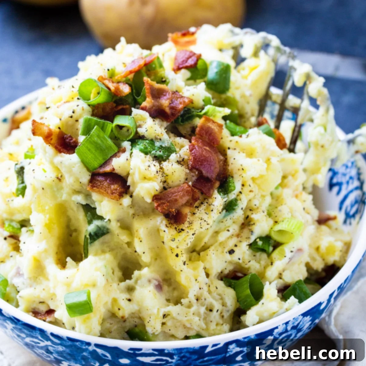 A beautifully presented serving bowl filled with creamy Bacon-Green Onion Mashed Potatoes, garnished with extra crispy bacon bits and finely sliced green onions.