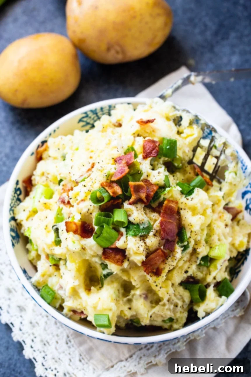 An overhead shot showcasing a blue bowl filled with creamy Bacon-Green Onion Mashed Potatoes, artfully arranged with additional whole potatoes and sprigs of green onion beside the bowl, emphasizing the fresh ingredients.