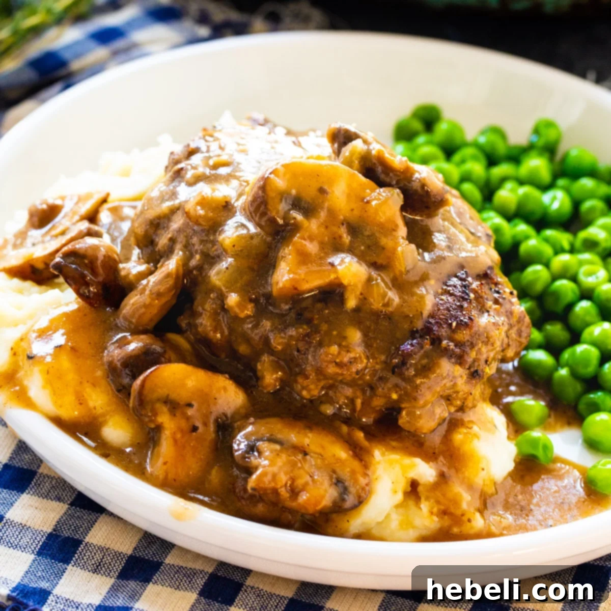 Hearty Hamburger Steak served over creamy mashed potatoes, generously topped with savory mushroom gravy, accompanied by fresh green peas.