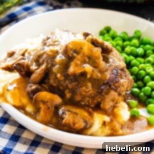 Hamburger Steak over mashed potatoes with peas, with savory mushroom gravy.