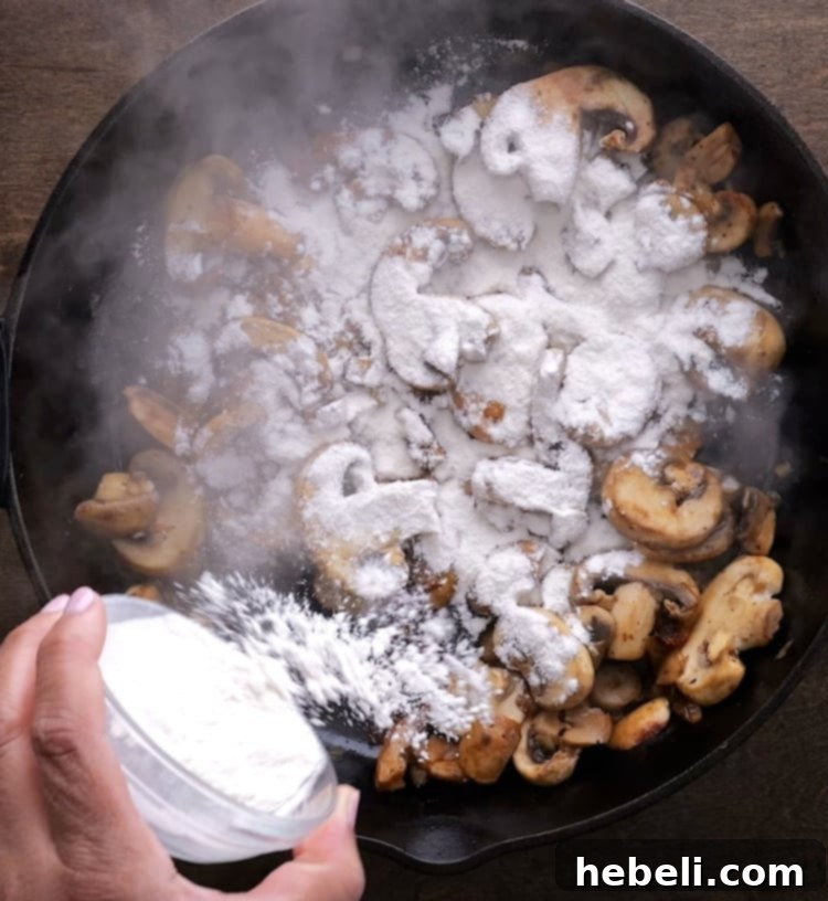 All-purpose flour being sprinkled over the sautéed mushrooms and onions in a skillet, stirred to create a gravy-thickening roux.