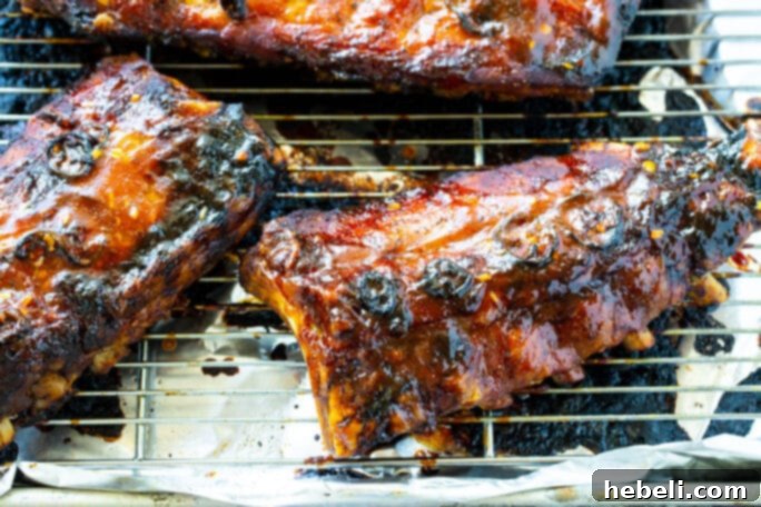 Sticky Sweet & Sour Ribs 3 Sweet and Sour Baby Back Ribs glistening on a wire rack over a baking sheet, freshly basted and ready for the final bake.