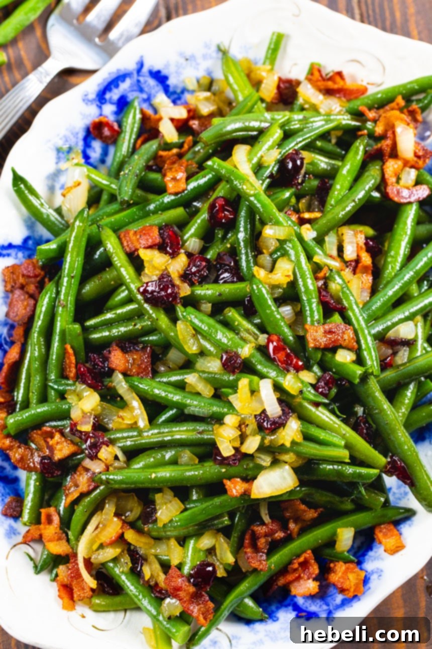 Overhead view of Maple-Glazed Green Beans on a serving platter, showcasing the rich glaze, crispy bacon, and bright cranberries.