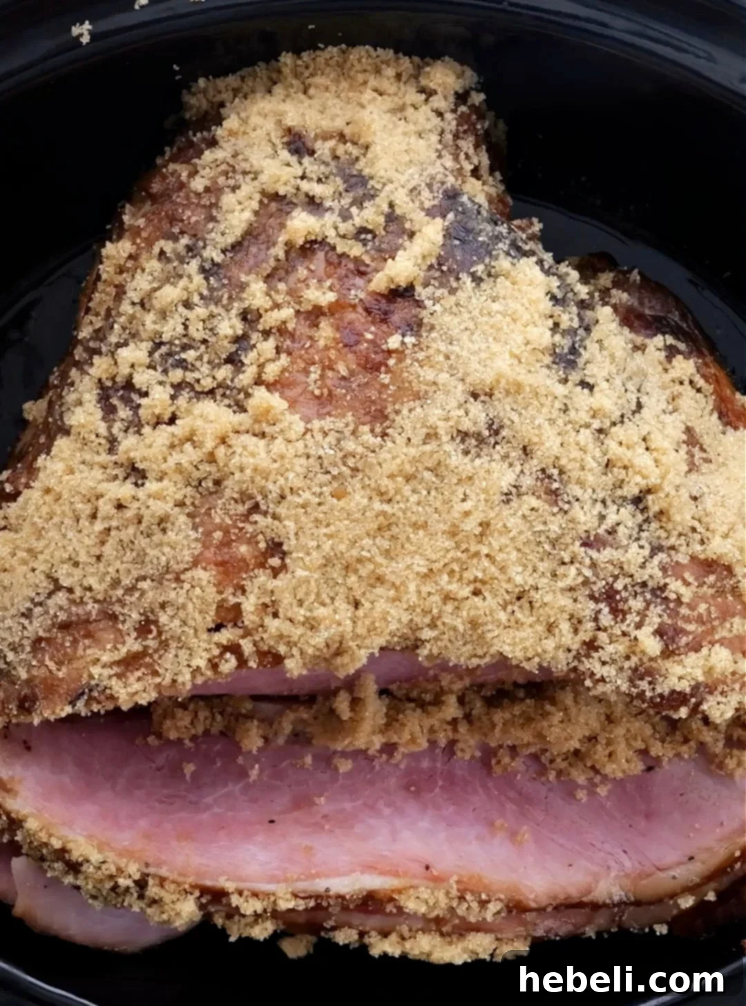 A fully cooked ham being rubbed with brown sugar after the first hour of slow cooking, ready for the final glaze.