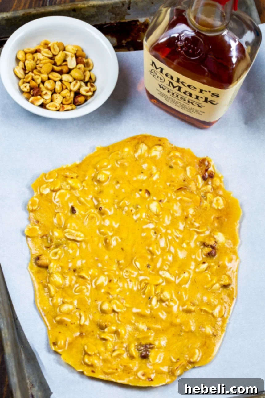 Unbroken sheet of golden Bourbon Peanut Brittle cooling on parchment paper, ready to be snapped into pieces.
