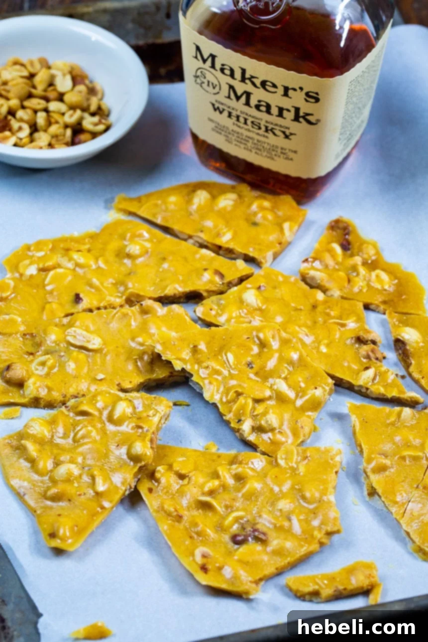 Arrangement of broken Bourbon Peanut Brittle pieces with a bottle of bourbon and a bowl of raw peanuts, hinting at the key ingredients.