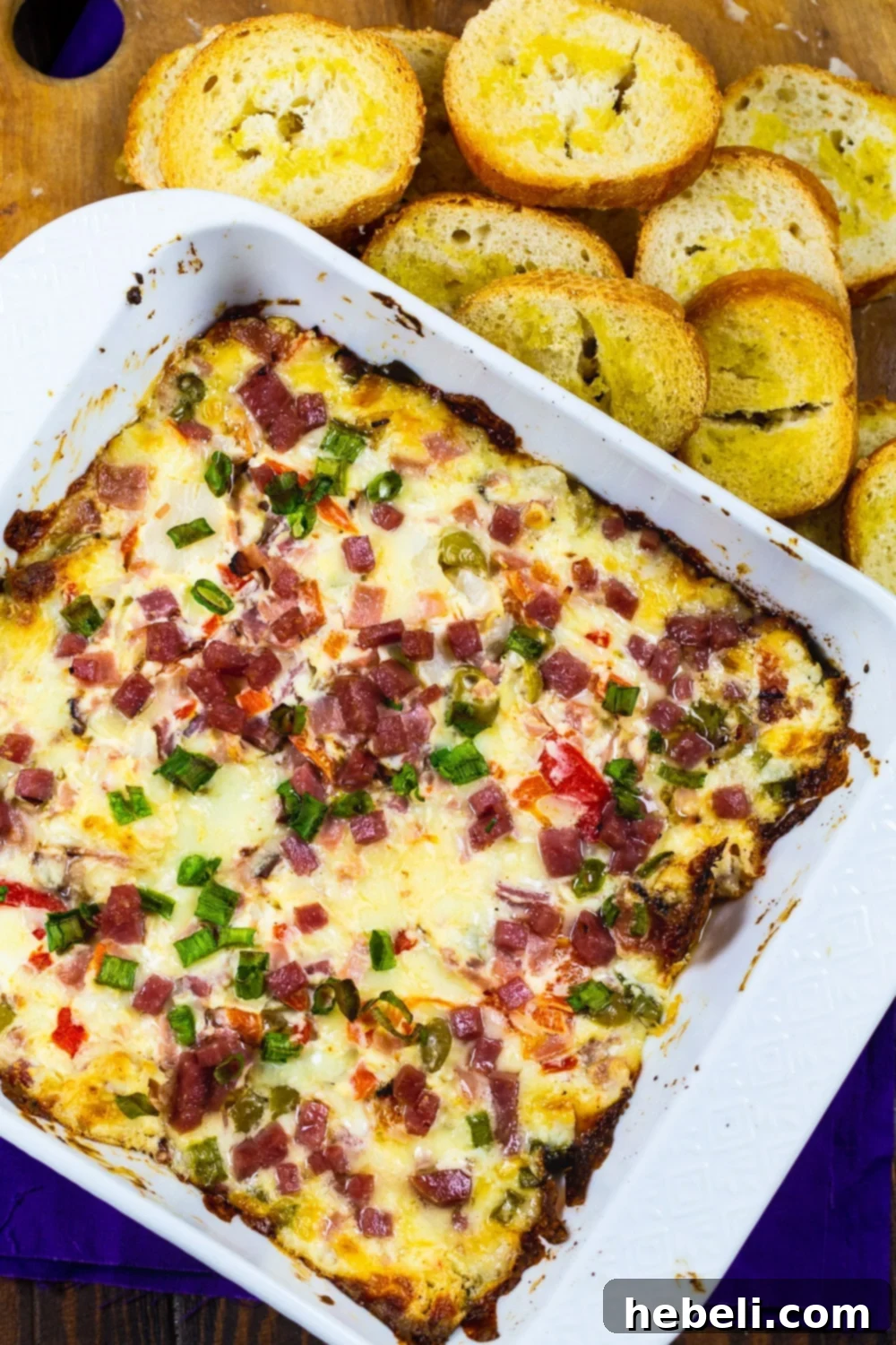 Muffaletta-Style Dip in a white baking dish, ready to be served, surrounded by golden baguette slices.