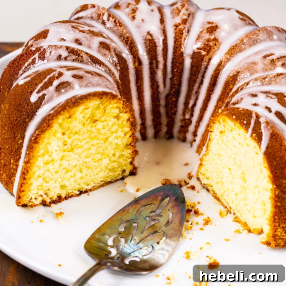 A beautifully glazed Five Flavor Pound Cake, three-quarters visible on a pristine white serving platter, ready to be sliced.