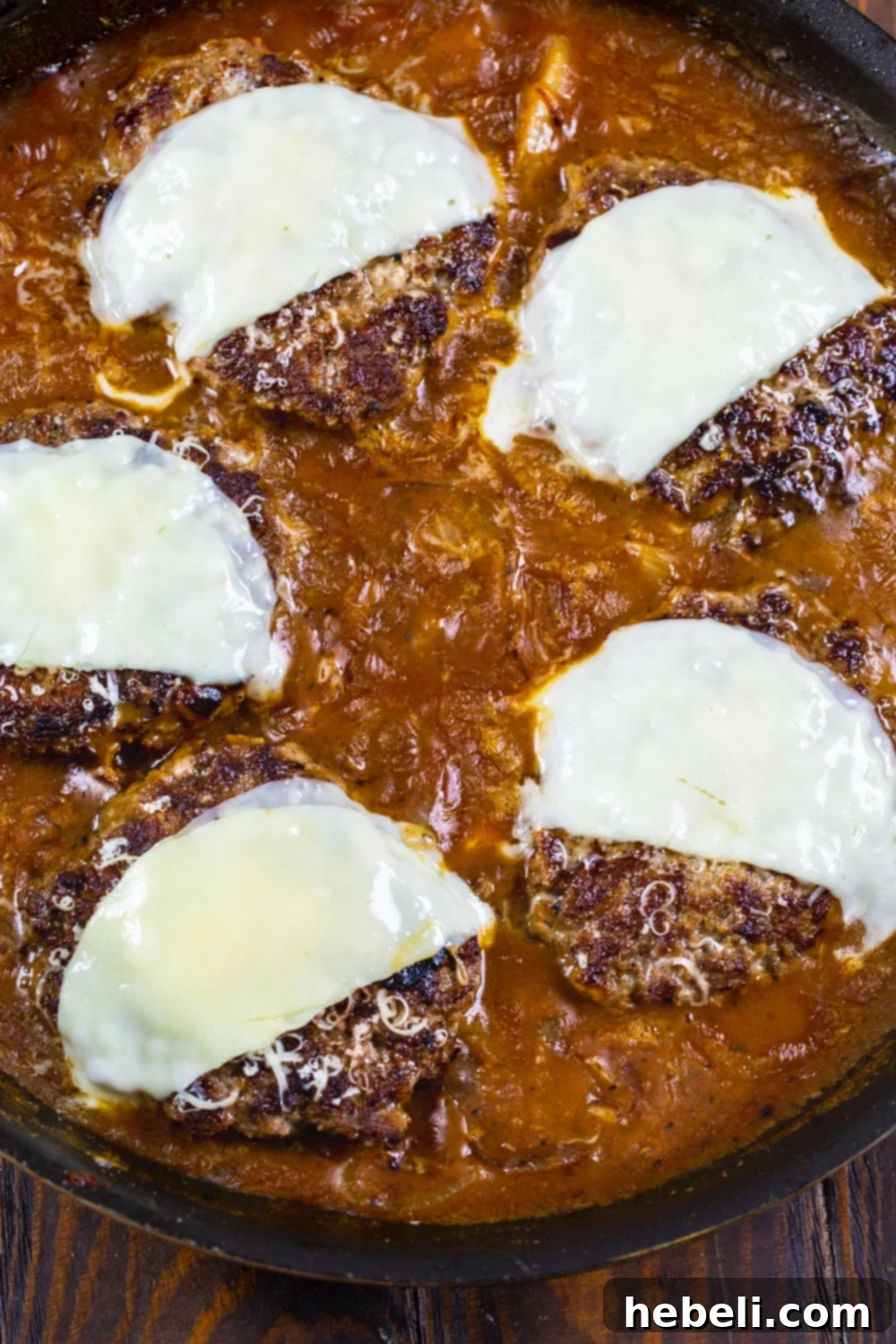 French Onion Smothered Salisbury Steak 3 Seared Salisbury Steak patties covered with a generous layer of melted cheese in a cast iron skillet.