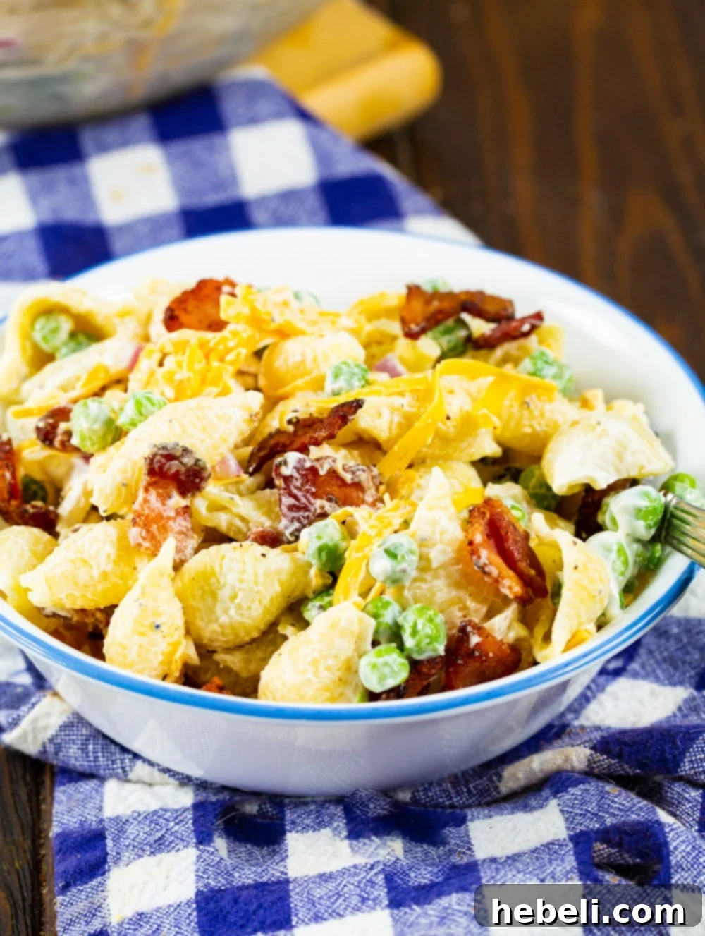 A perfectly portioned serving of Creamy Pasta Salad with Peas and Bacon in a pristine white ceramic bowl, garnished with a sprig of fresh parsley, ready for a delicious meal.