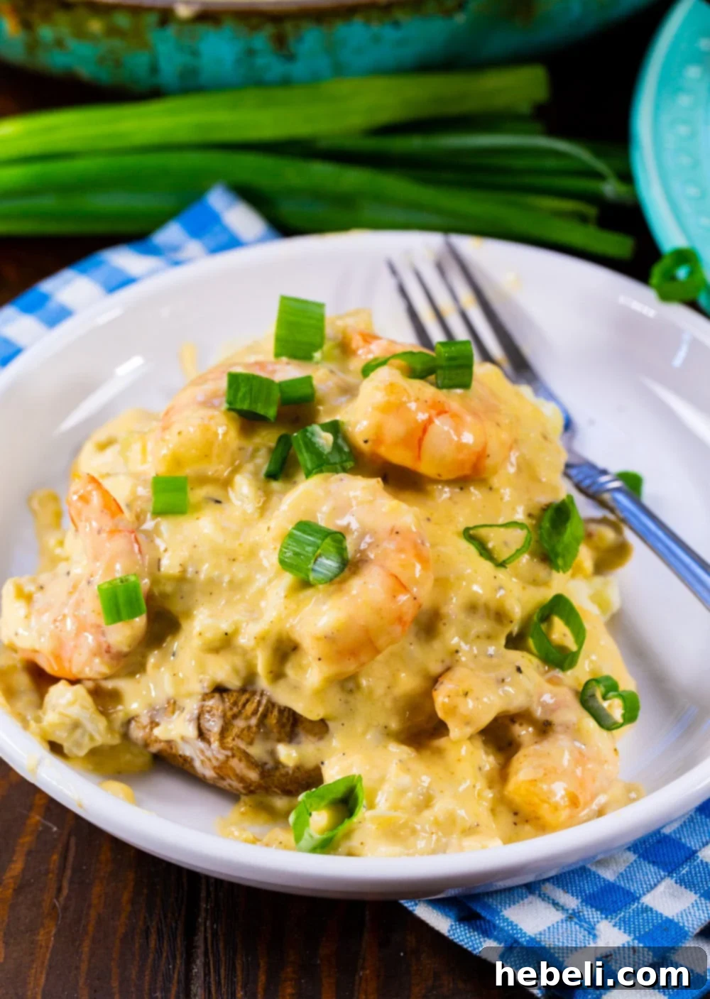 Stuffed Potato topped with cheesy seafood sauce and sliced green onions on a white plate.