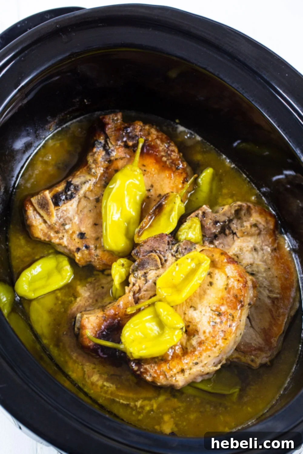 Slow Cooker Mississippi Magic Chops 3 Raw Mississippi Pork Chops seasoned and arranged with butter and pepperoncini peppers inside a slow cooker, ready for cooking.