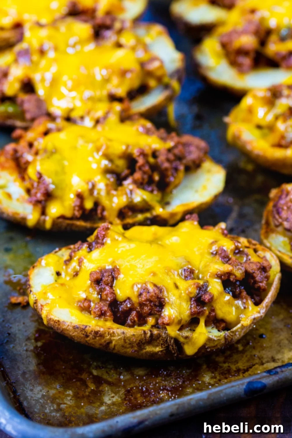 Crispy potato skins loaded with melted cheddar cheese on a baking sheet, ready for the next step of filling.