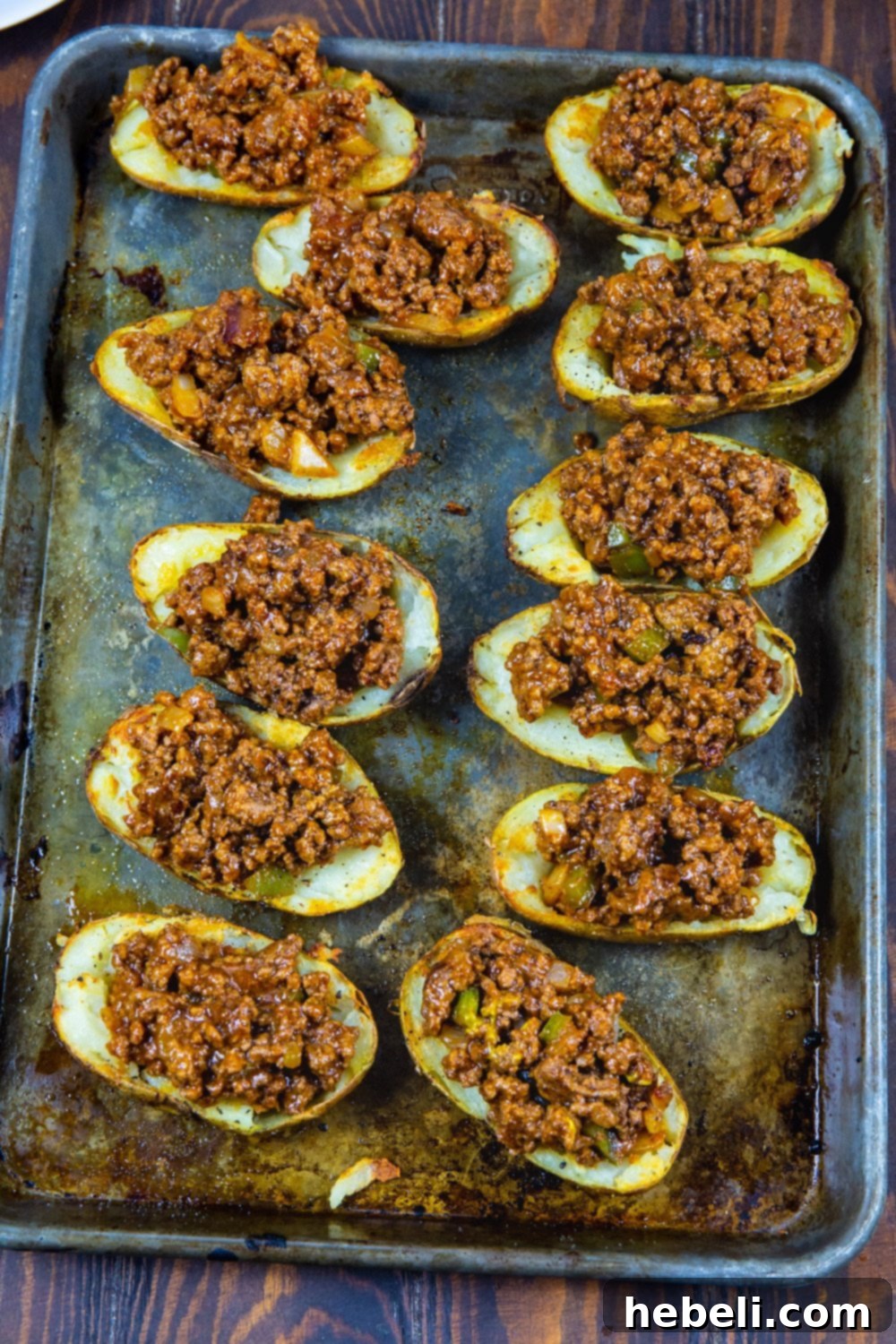 Golden-brown potato halves generously filled with a rich, savory sloppy joe mixture, awaiting their final cheese topping.